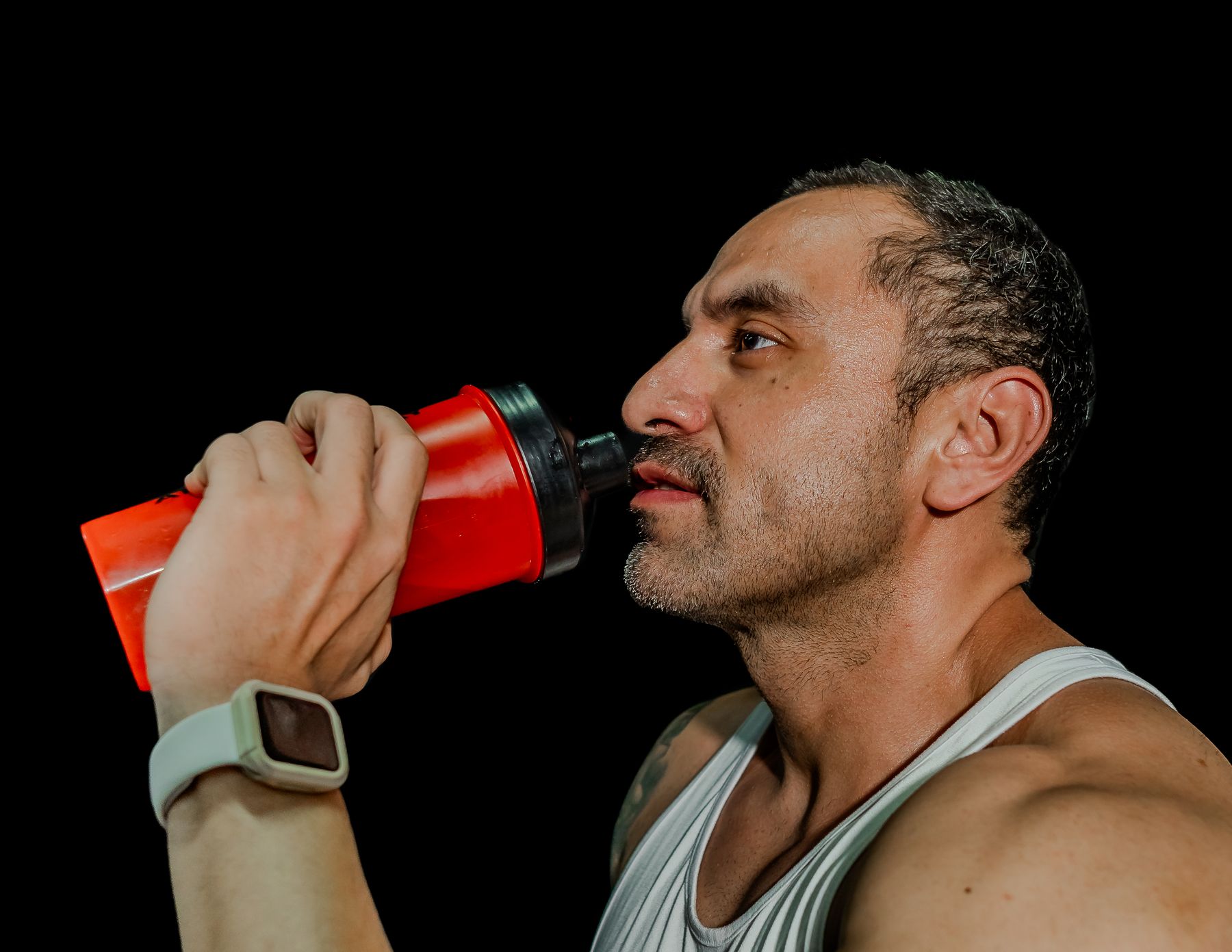 Homme en débardeur buvant dans un shaker rouge sur fond noir